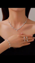 Silver jewelry set including necklace, bracelet, and ring on a model against a neutral background